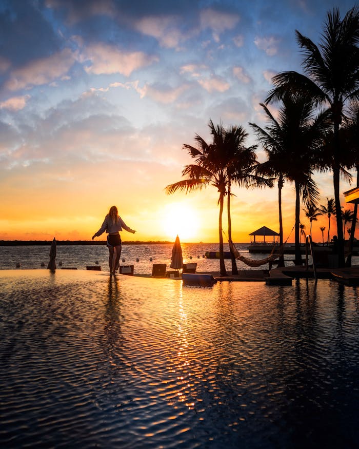 Relaxing evening scene with a woman by a tropical pool at sunset, perfect for vacation promotion.