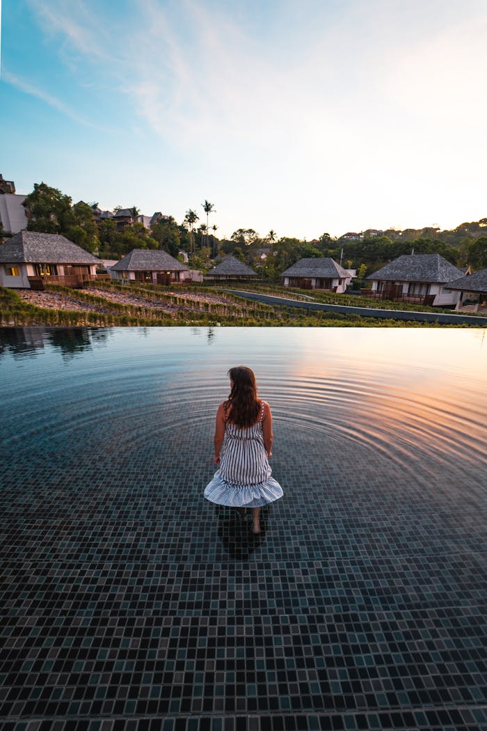 gallery-3 A woman in a white dress stands in an infinity pool at a Thai resort during sunset.